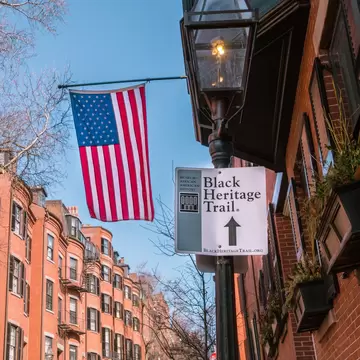Boston, MA, US-June 10, 2023: Black Heritage Trail sign in Boston's historic Beacon Hill nieghborhood with American flag and 19th century brick buildings in background., License Type: media, Download Time: 2024-09-10T06:43:40.000Z, User: oneseven7891, Editorial: true, purchase_order: 56530, job: Global Publishing WIP, client: Pocket Boston 6, other: Dominic Allen