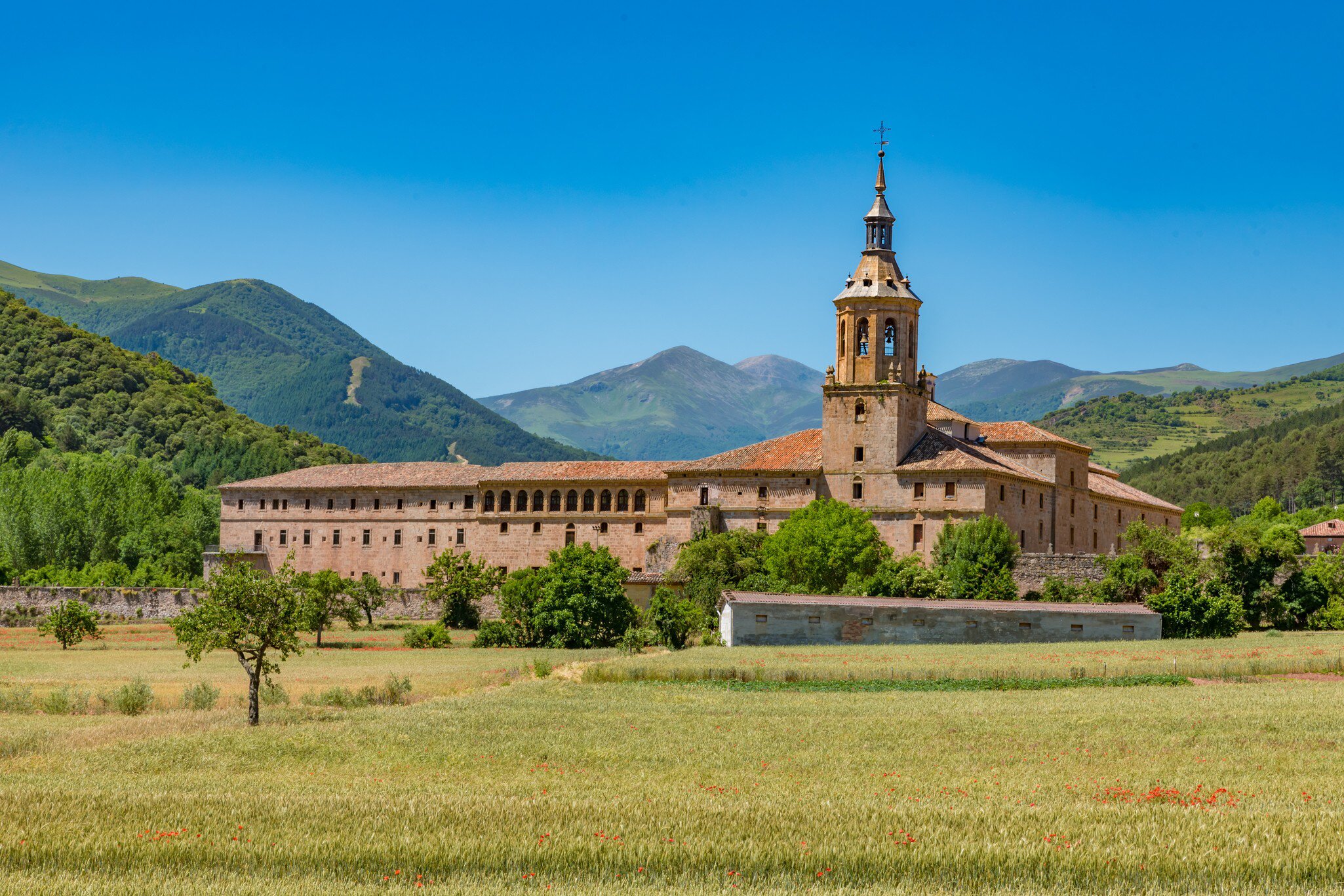View of the Monasterio de Yuso in San Millán de la Cogolla, Spain, surrounded by fields and mountains.