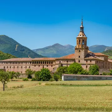 View of the Monasterio de Yuso in San Millán de la Cogolla, Spain, surrounded by fields and mountains.