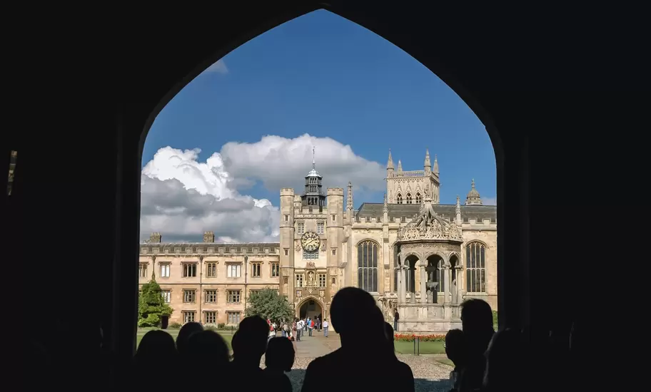 Cambridge: Trinity College Great Court, clock tower and fountain seen past silhouetted visitors in an arch
