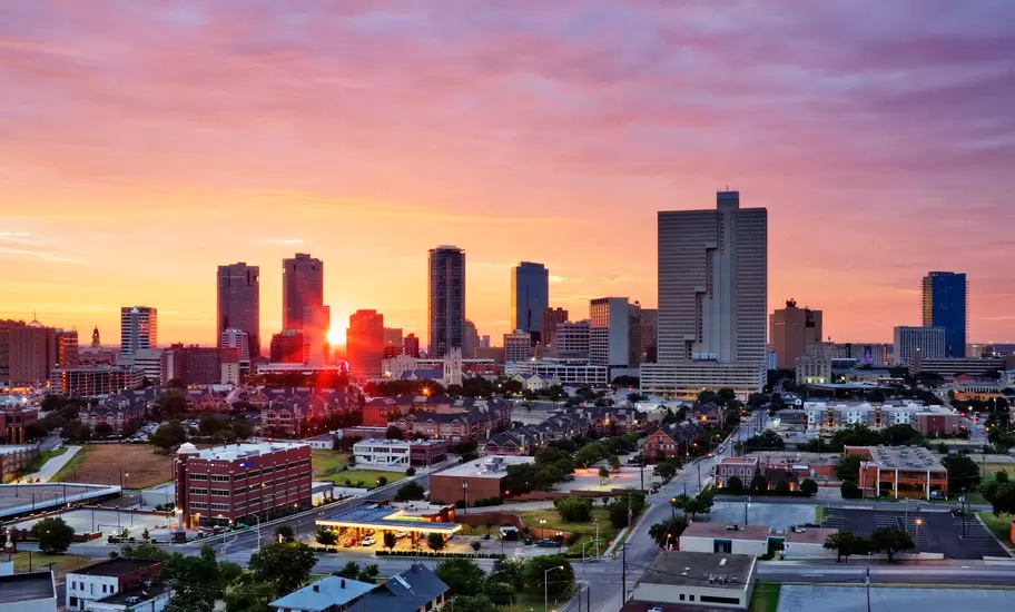 Downtown Fort Worth skyline silhouetted against a pink and orange sunrise, with low-rise streets and townhouses below