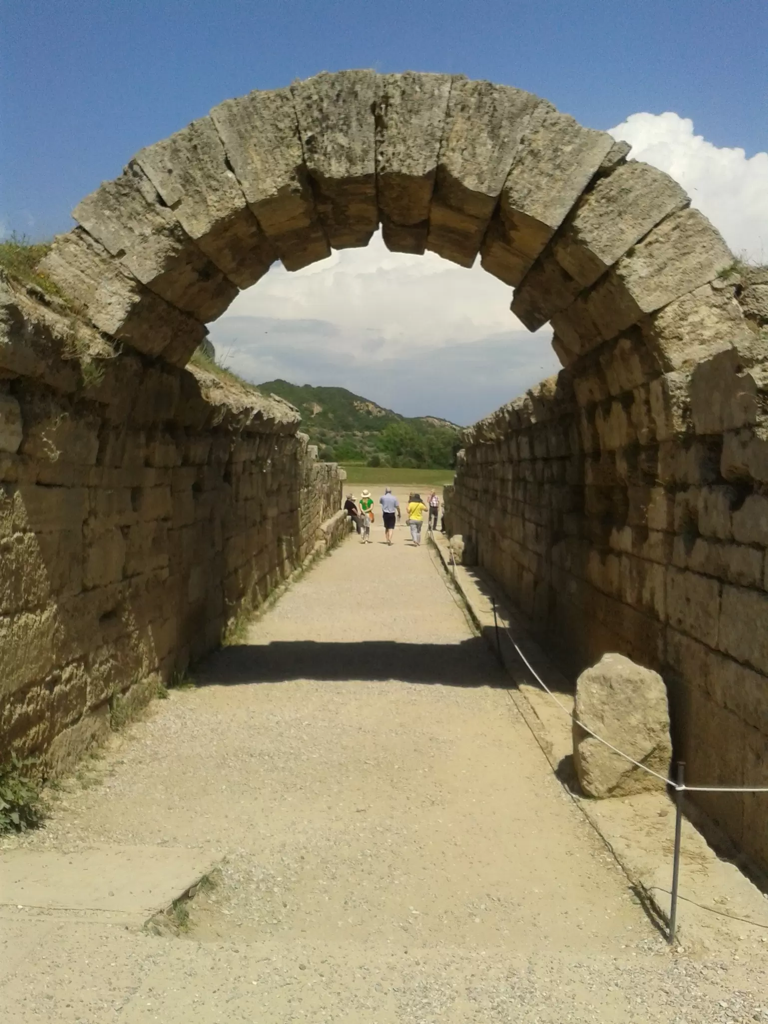 Crowds walk under a stone arched entrance into the stadium where Olympic events were originally held in Ancient Olympia, Greece.