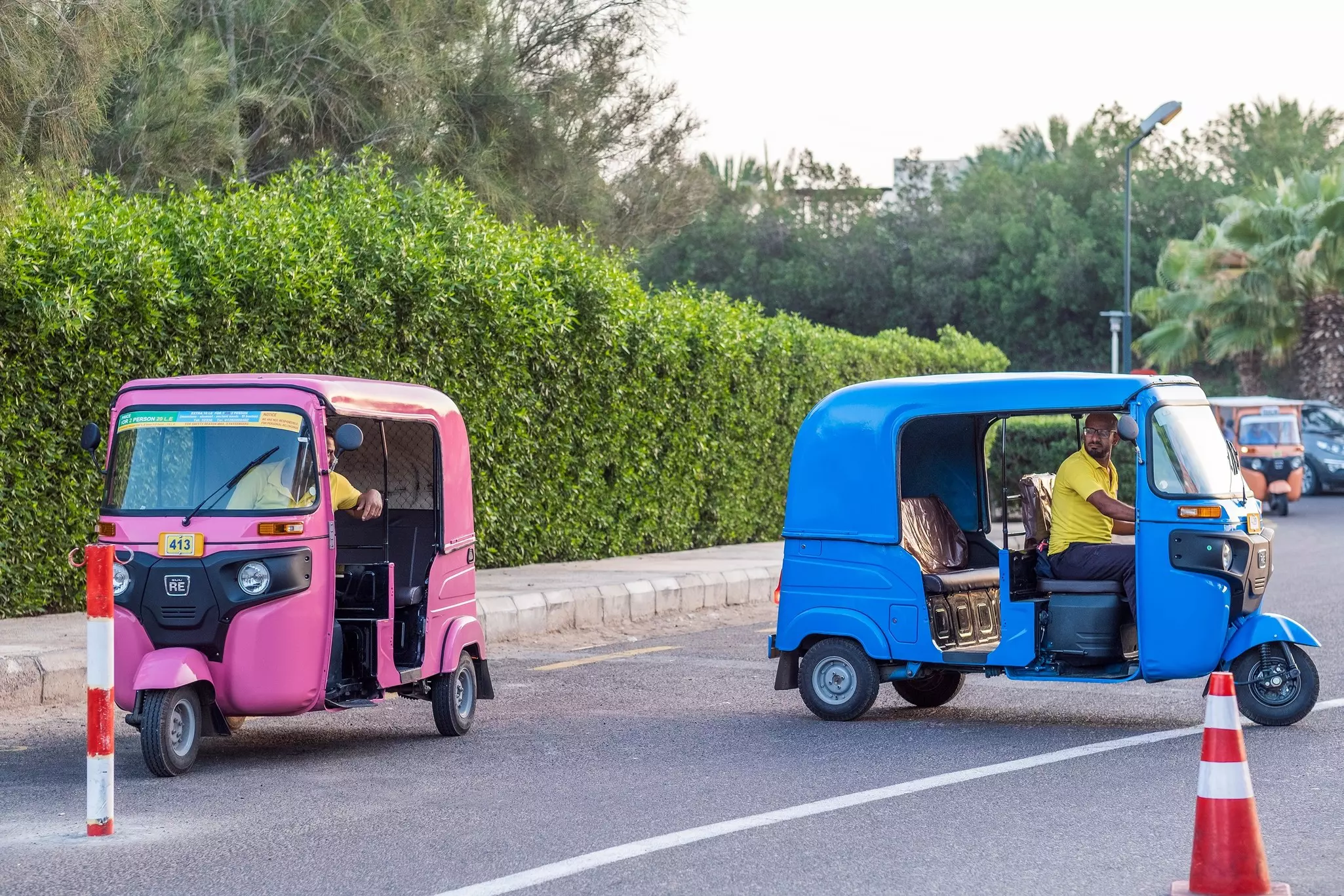 A pink tuk-tuk and a blue tuk-tuk on the street