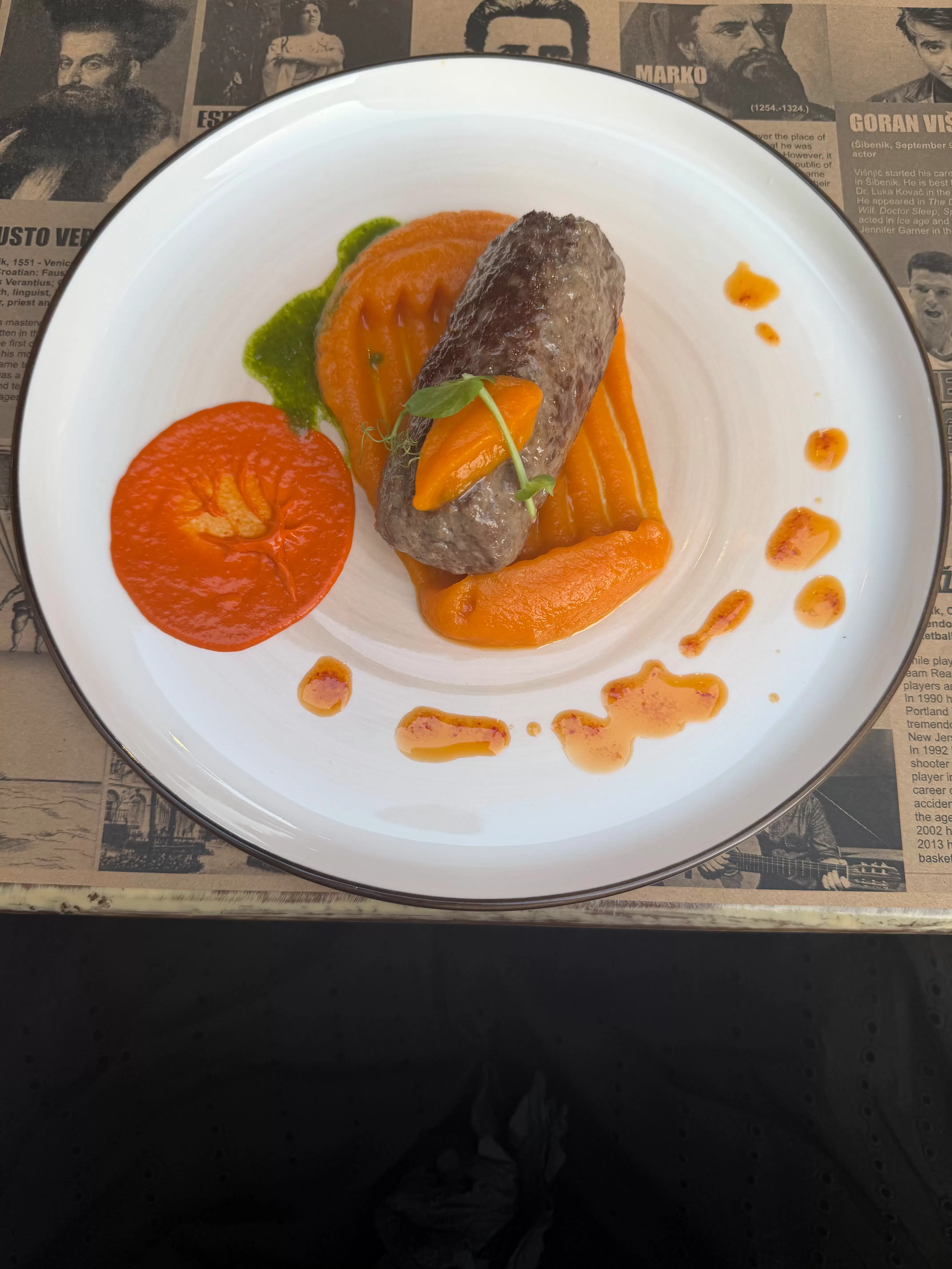 Closeup of a white plate with bright orange sweet potato sauce topped with a log of lamb. 