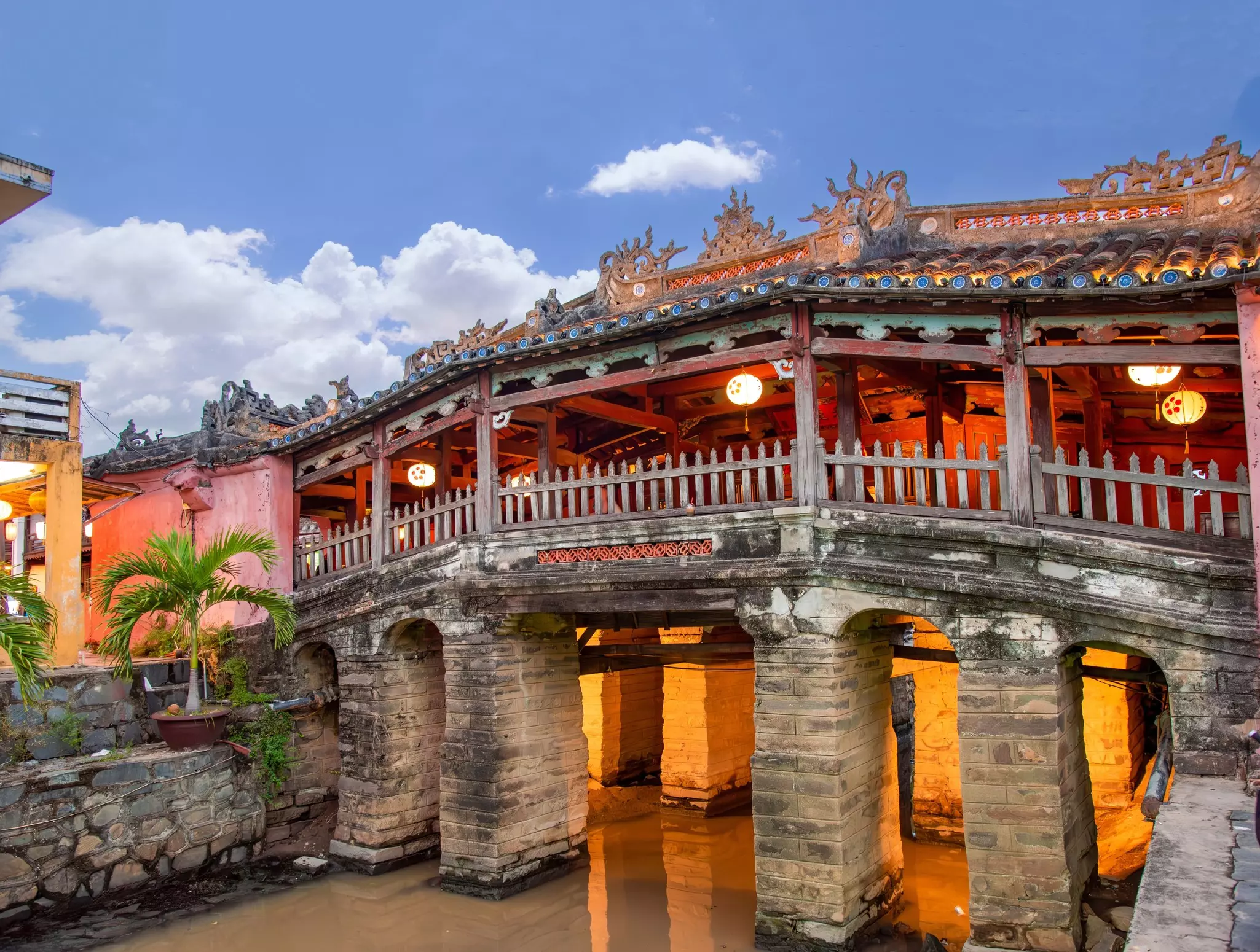 A bridge over a narrow canal has stone pillars and an elaborate canopy.