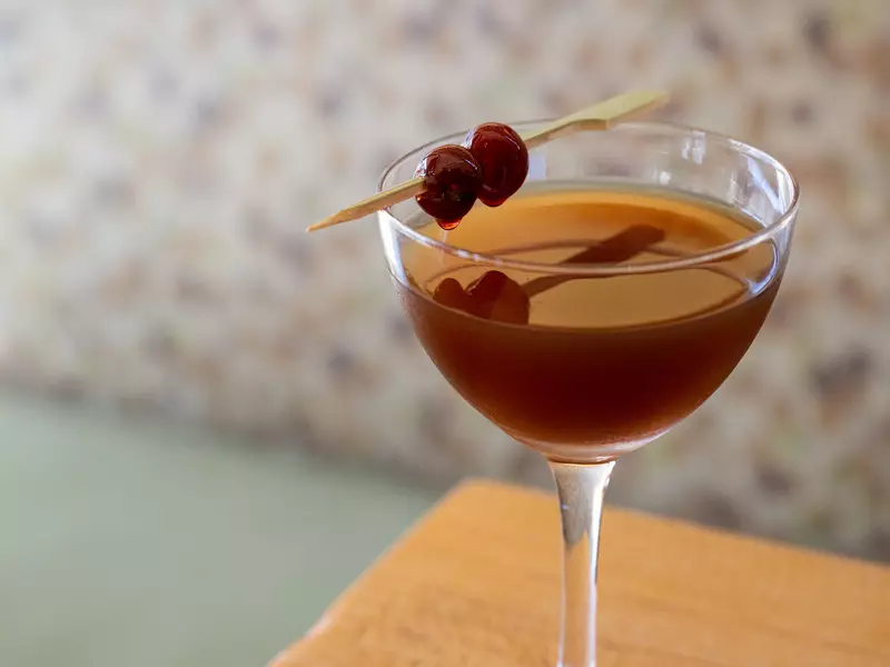 thick Manhattan with cherries in a martini glass on a wooden table.