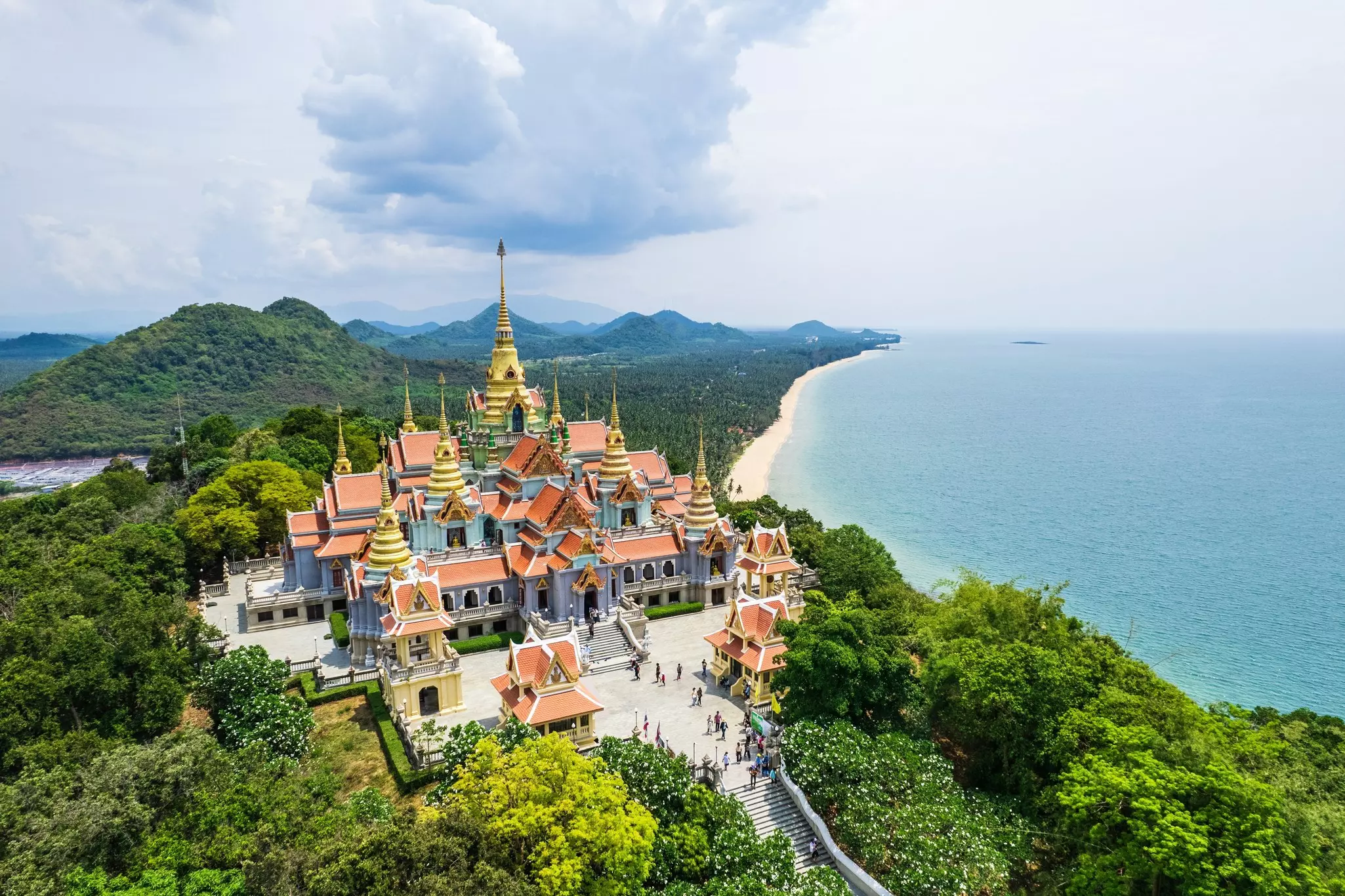 A large and colorful Buddhist temple perched on a lush, green mountaintop on the shore of a beach