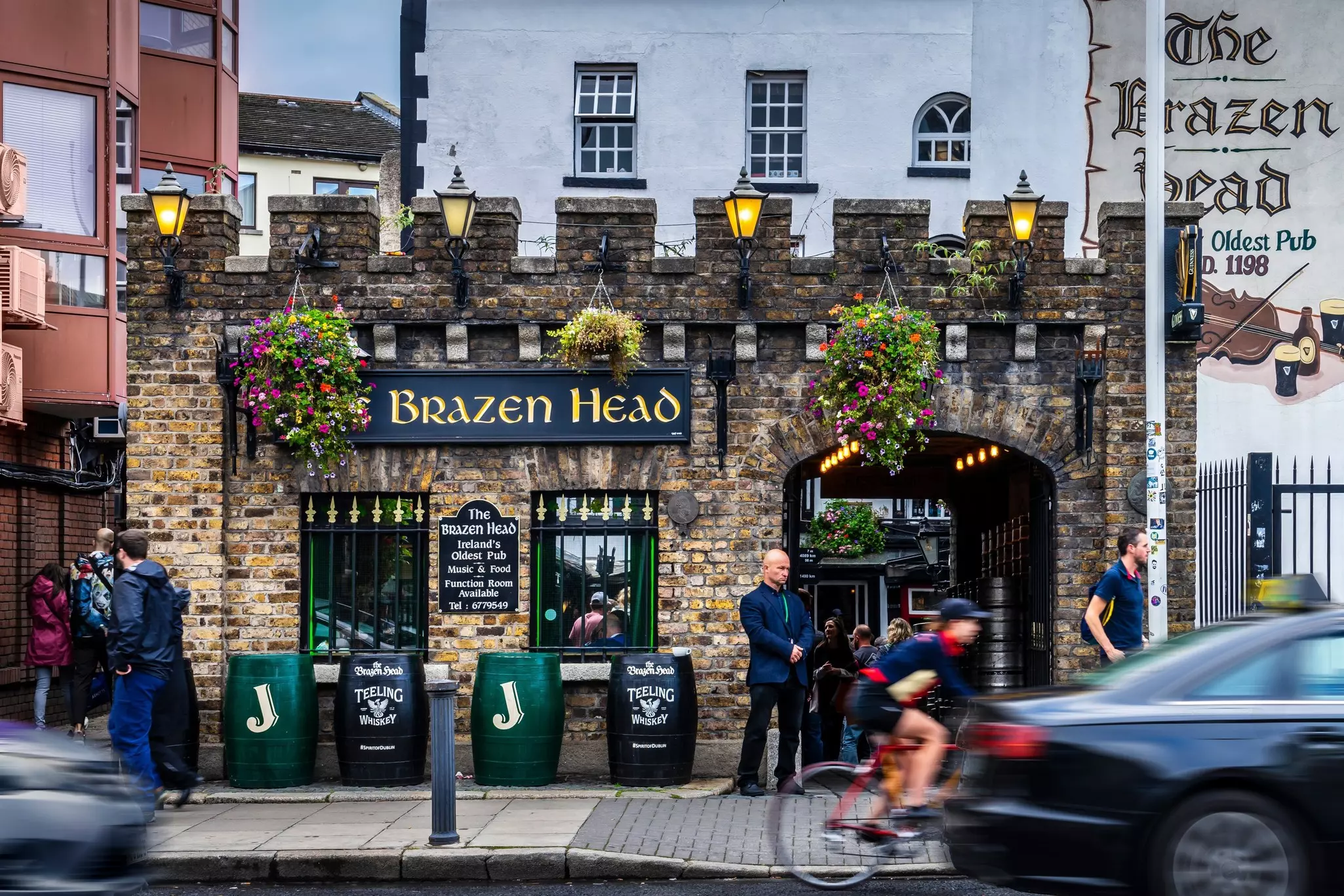 Exterior of The Brazen Head, the oldest pub in Dublin, a brick building with barrels outside and hanging plants near the top
