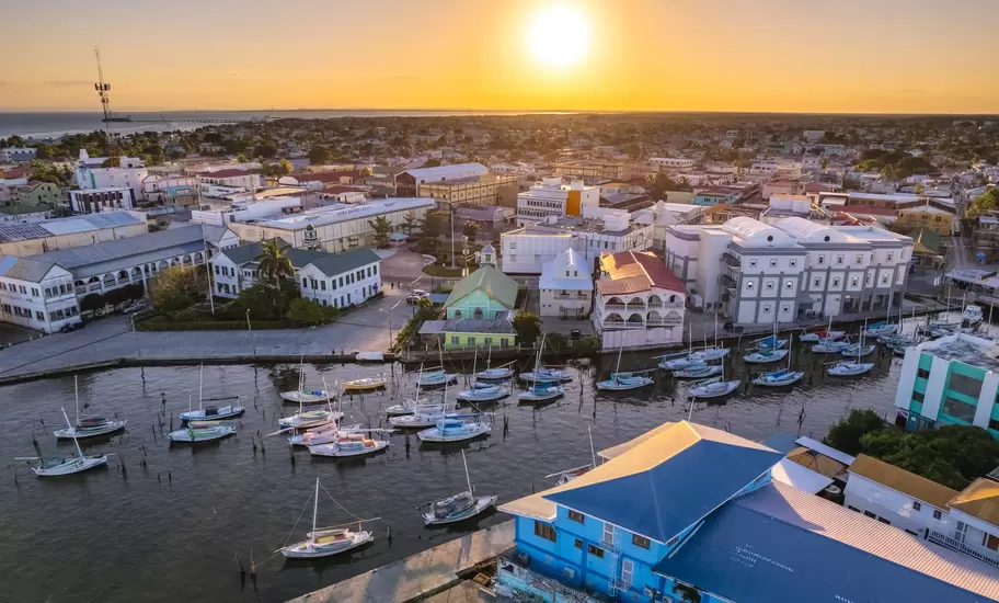 An aerial view of a waterfront in a city at sunset. Buildings with porches line the waterfront, while sailboats are moored in the water.