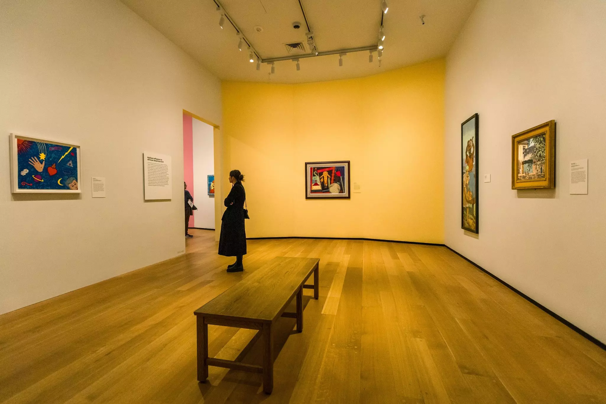 A woman stands alone in a gallery of a museum looking at paintings.