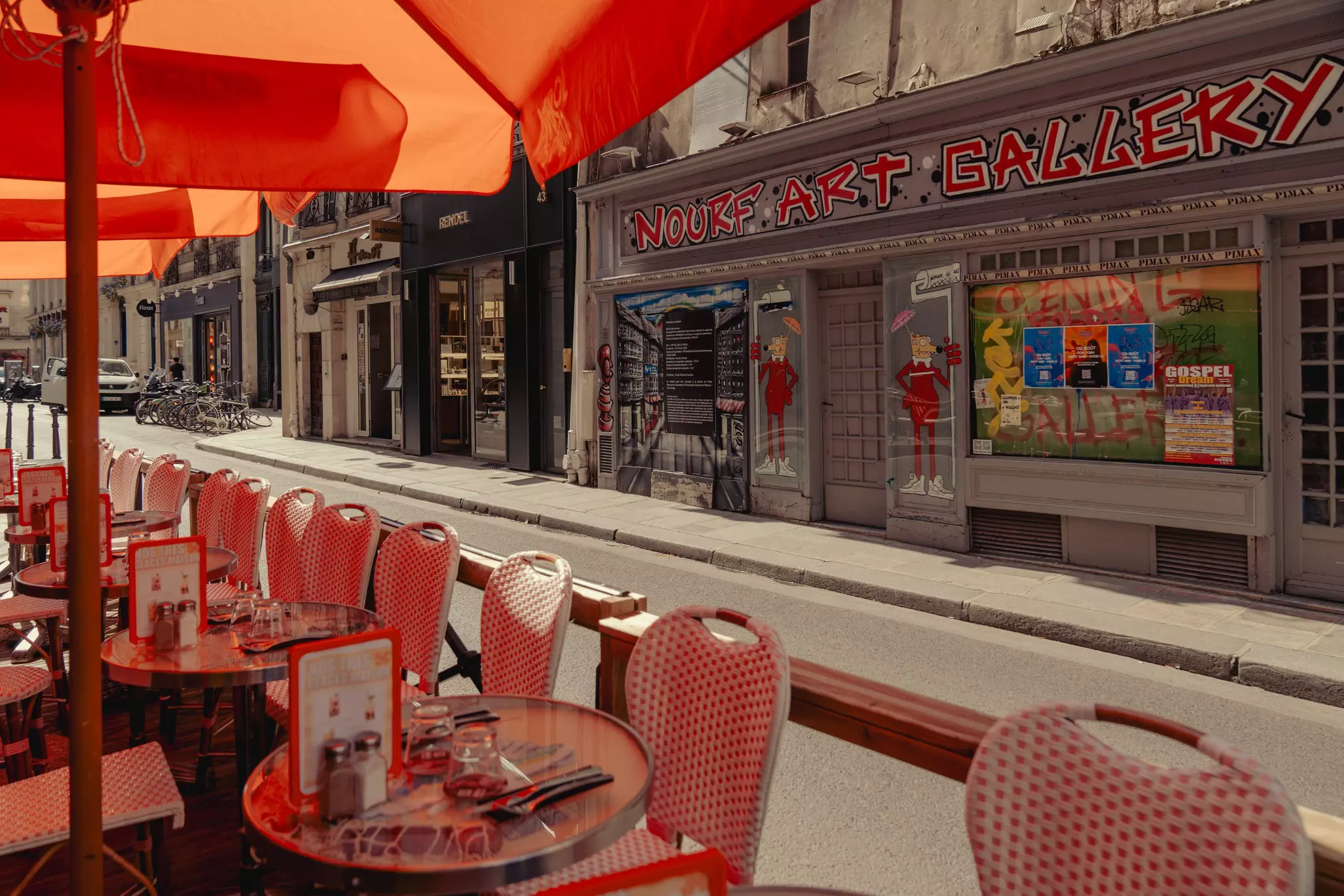 Red tables under red umbrellas at a sidewalk cafe on an empty street.