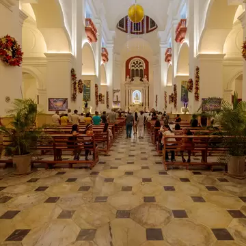 Church nave with octagonal marble floor, wooden pews, red carved balconies and hanging Christmas baubles leading to the altar