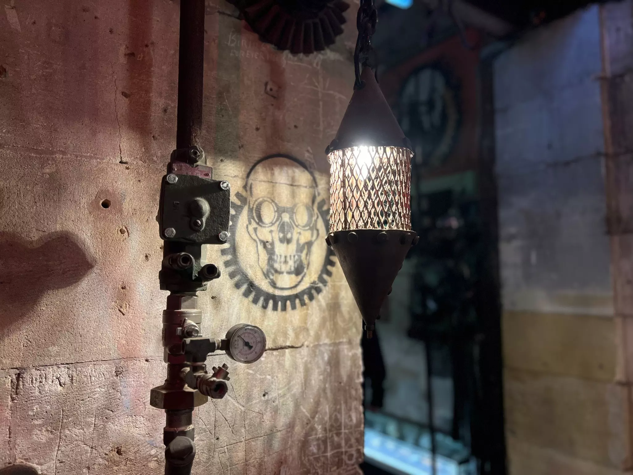 A dark room lit by a hanging lantern, revealing a skull motif painted on the wall.
