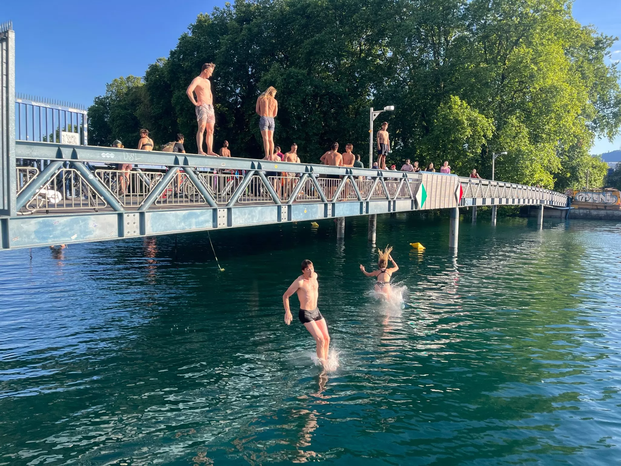 People stand on a pedestrian bridge and jump into the river below
