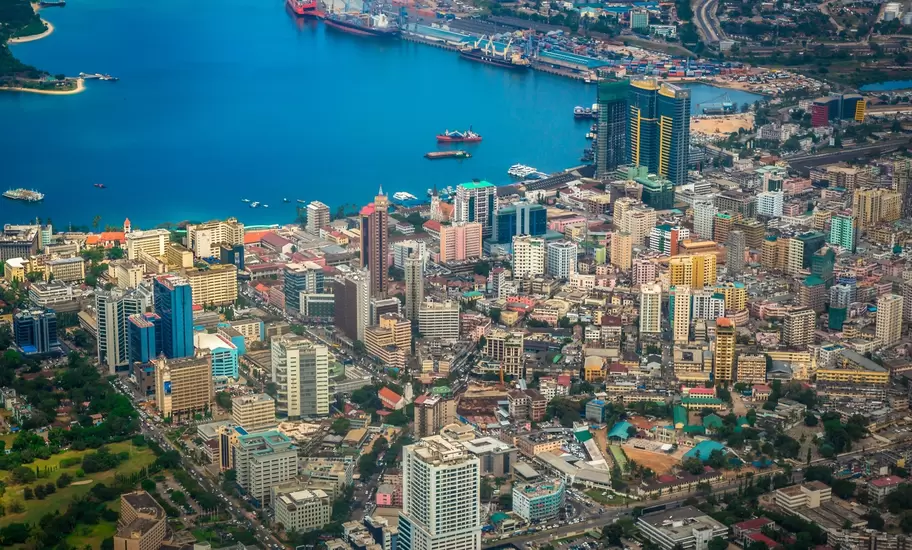 Aerial view of downtown Dar es Salaam's high-rises along the blue harbour, with port cranes and cargo ships beyond