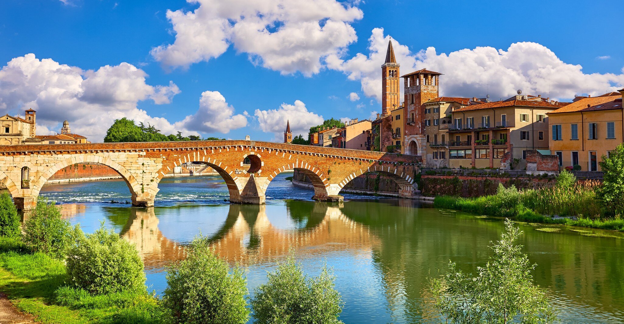 A five-arched stone and brick bridge over a green river, hills rising behind.