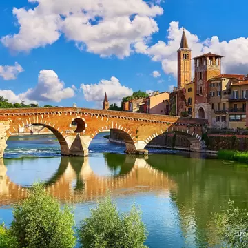 A five-arched stone and brick bridge over a green river, hills rising behind.