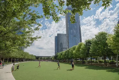 DALLAS, TX, USA-MAY 26, 2018:Klyde Warren Park, a 5.2-acre public park in downtown Dallas, Texas. People playing sport on green lawn grass under sunny day cloud blue sky. Live oak tree and skyscraper