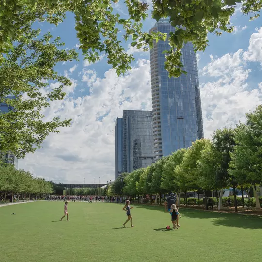 DALLAS, TX, USA-MAY 26, 2018:Klyde Warren Park, a 5.2-acre public park in downtown Dallas, Texas. People playing sport on green lawn grass under sunny day cloud blue sky. Live oak tree and skyscraper