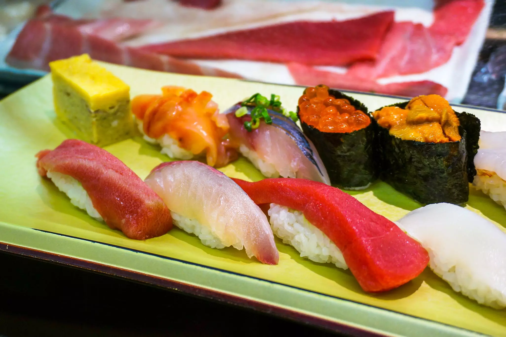 Omelette, salmon roe, sea urchin uni, tuna, squid and yellowtail sushi on rice on a plate, with some pieces wrapped in seaweed