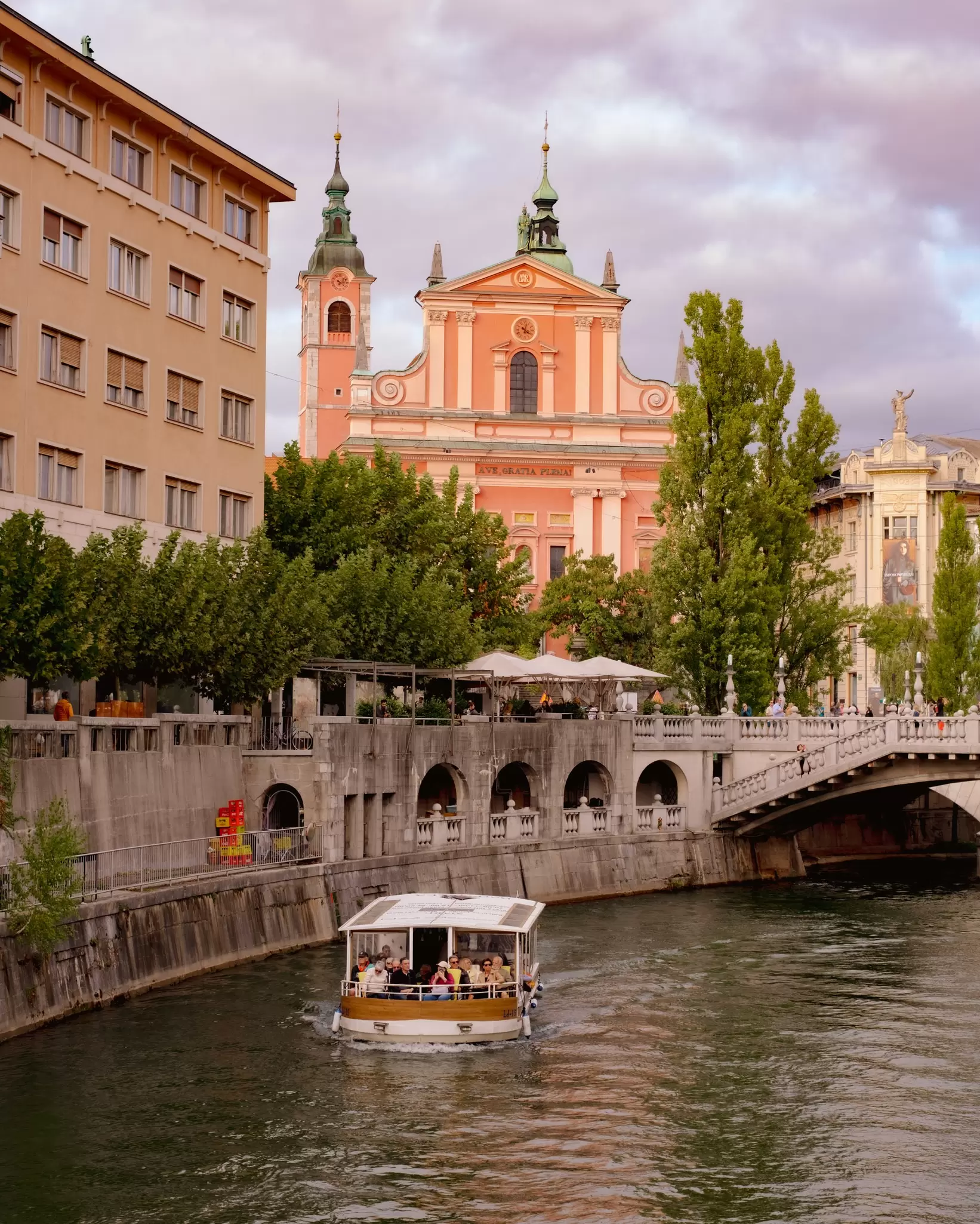 A tourist boat sailing along a river through a city center with ornate buildings in the background.