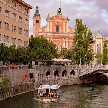 A tourist boat sailing along a river through a city center with ornate buildings in the background.