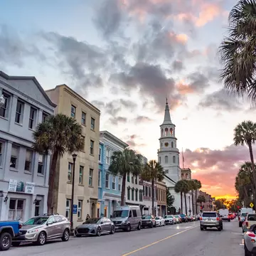 A historic street of a city with a church spire under the array of colors in the sky at sunset.