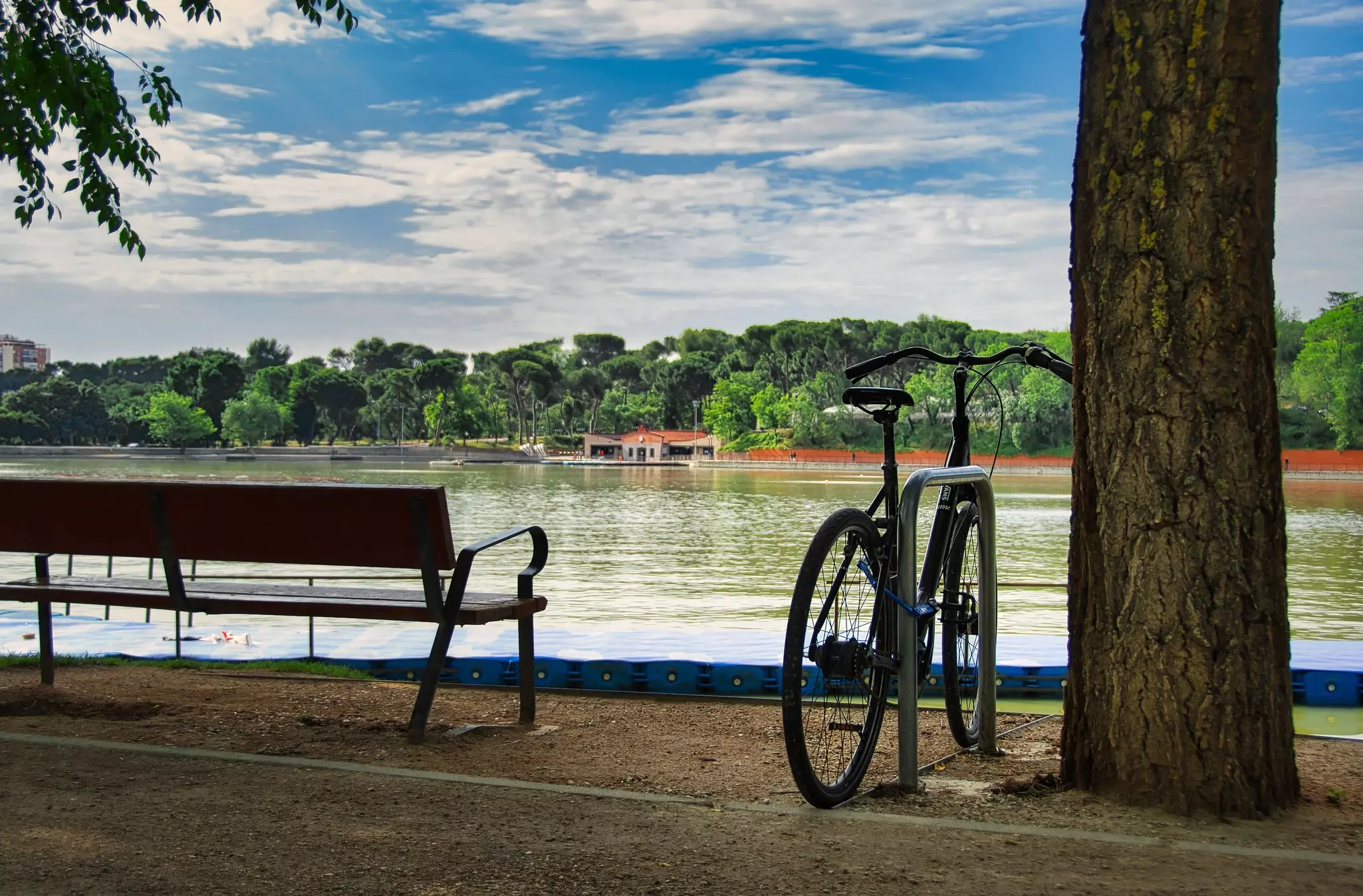 A bike locked to a rack by a wooden bench next to a pond in Madrid.