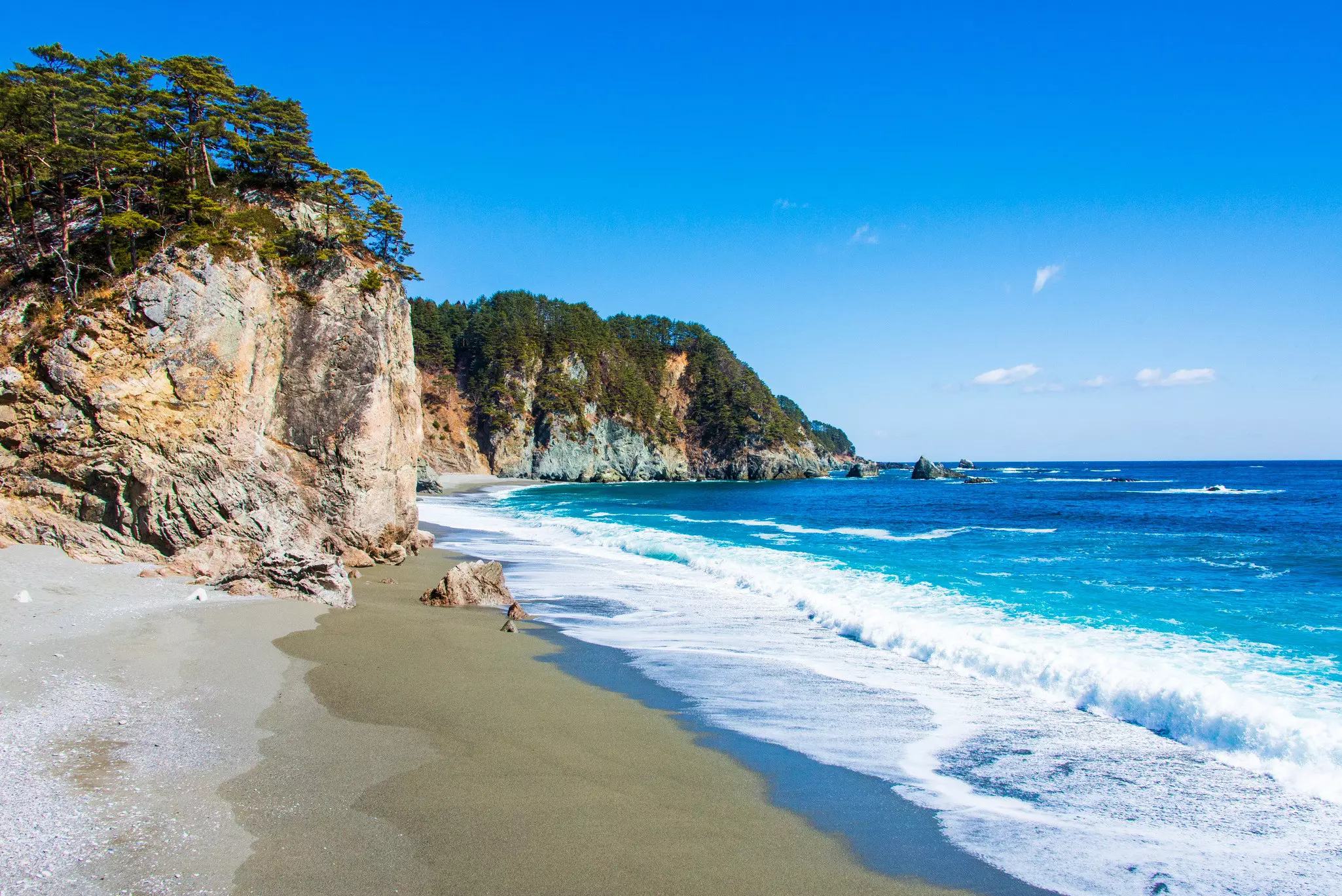 A sandy beach backed by tree-topped cliffs and lapped by turquoise waves