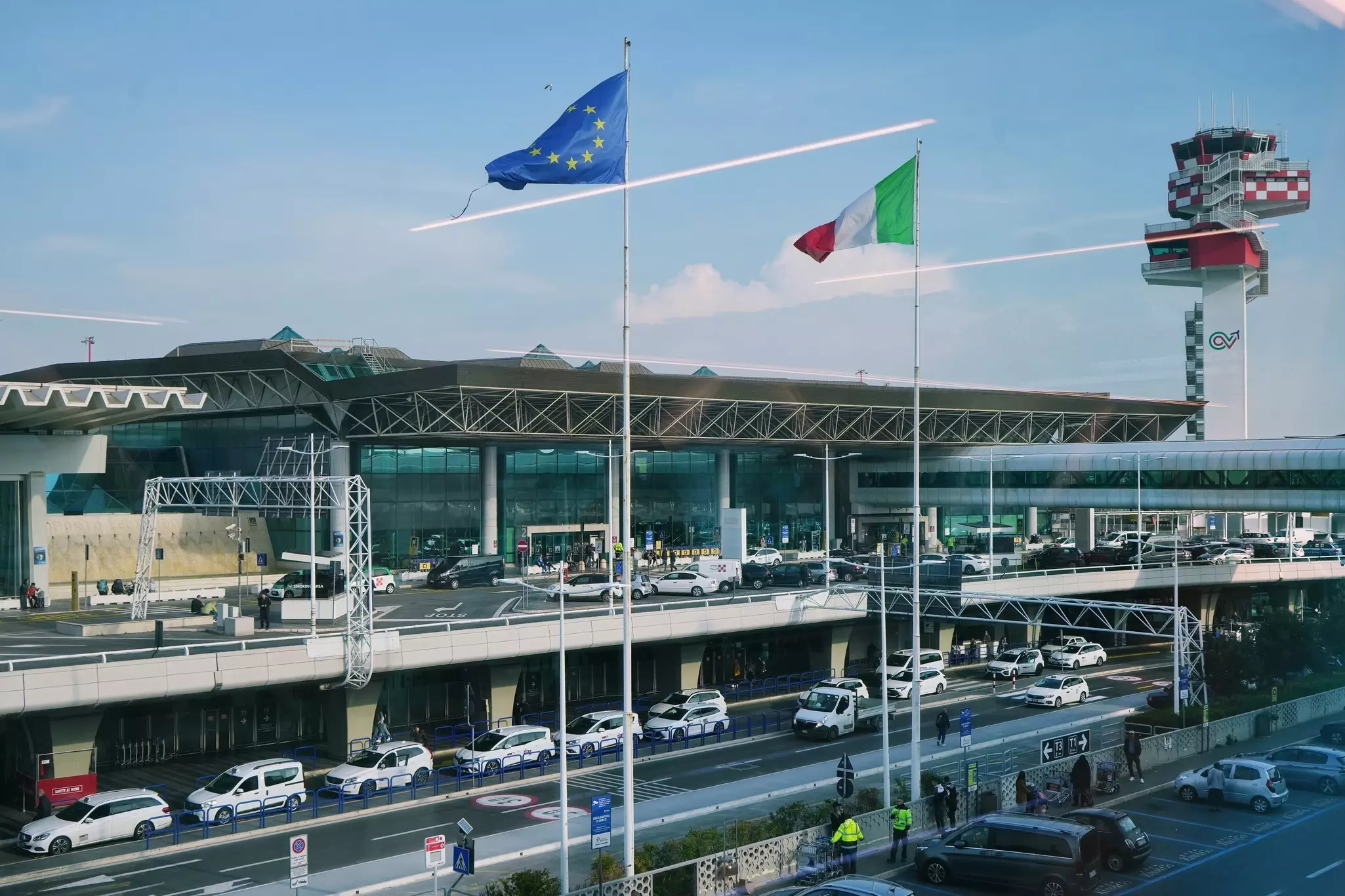 The exterior of an airport terminal with two floors, each with white taxis lined up outside.