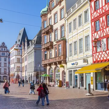 Shoppers on the Hauptmarkt in Trier, Germany, below half-timbered and pastel facades and the tower of St Gangolf