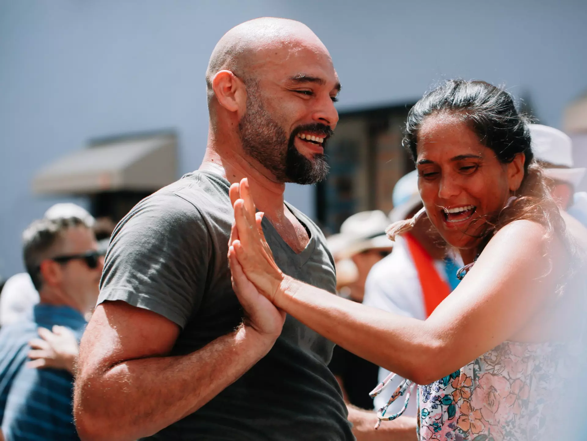 A man and a woman touch hands as they dance to salsa music outside with a group of people.