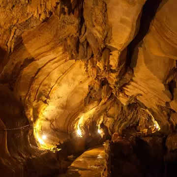 A cave interior of folded, layered rock lit warm gold, with a narrow walkway curving away through it.