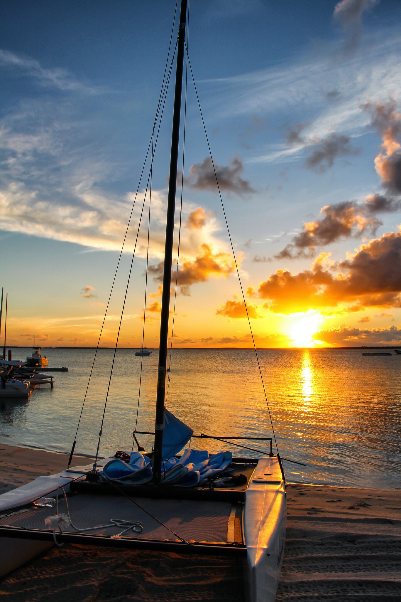 A small catamaran docked on a sandy beach at sunset, with the ocean glowing orange in the end-of-day light.