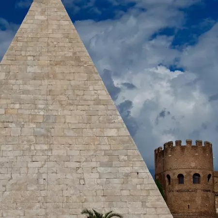A pyramid in Rome is flanked by a palm tree and a castle turret.