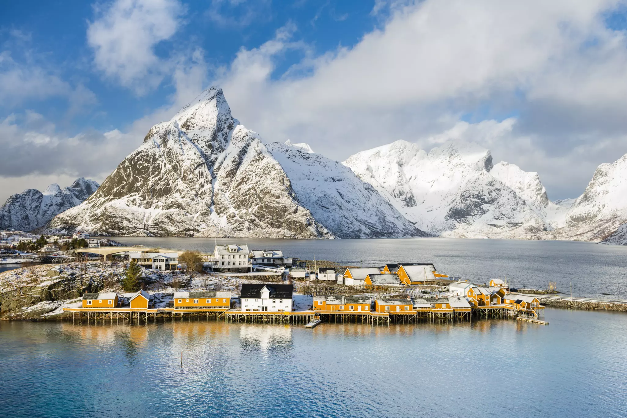 Rorbu huts on clear blue water with mountains behind in the Lofoton islands, Norway.