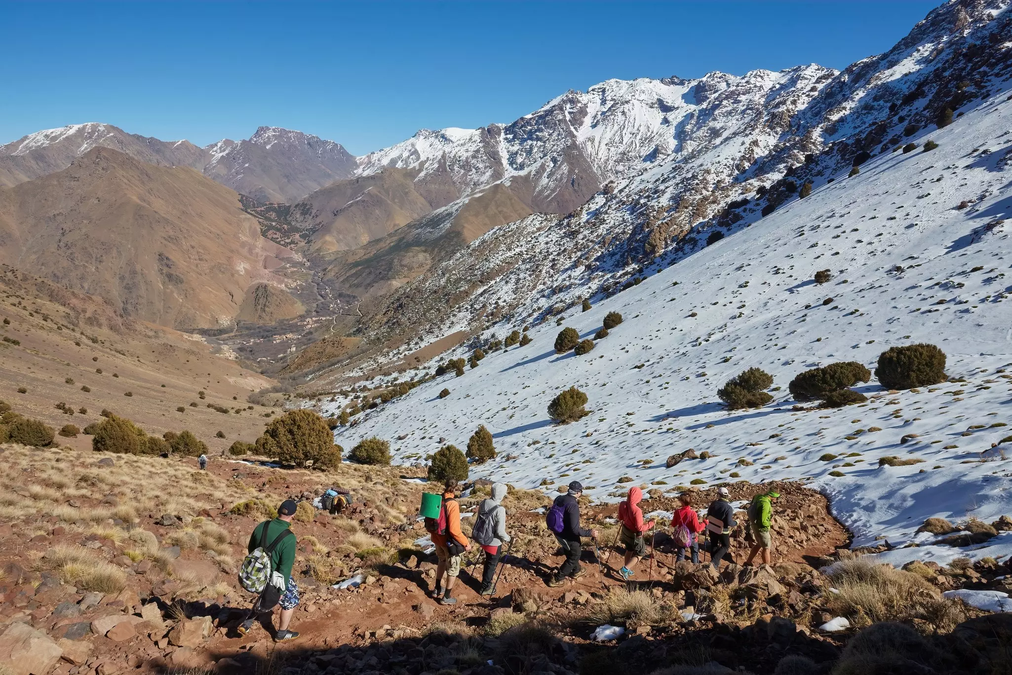 A group of hikers follow a guide down a path through a snowy mountainous region.