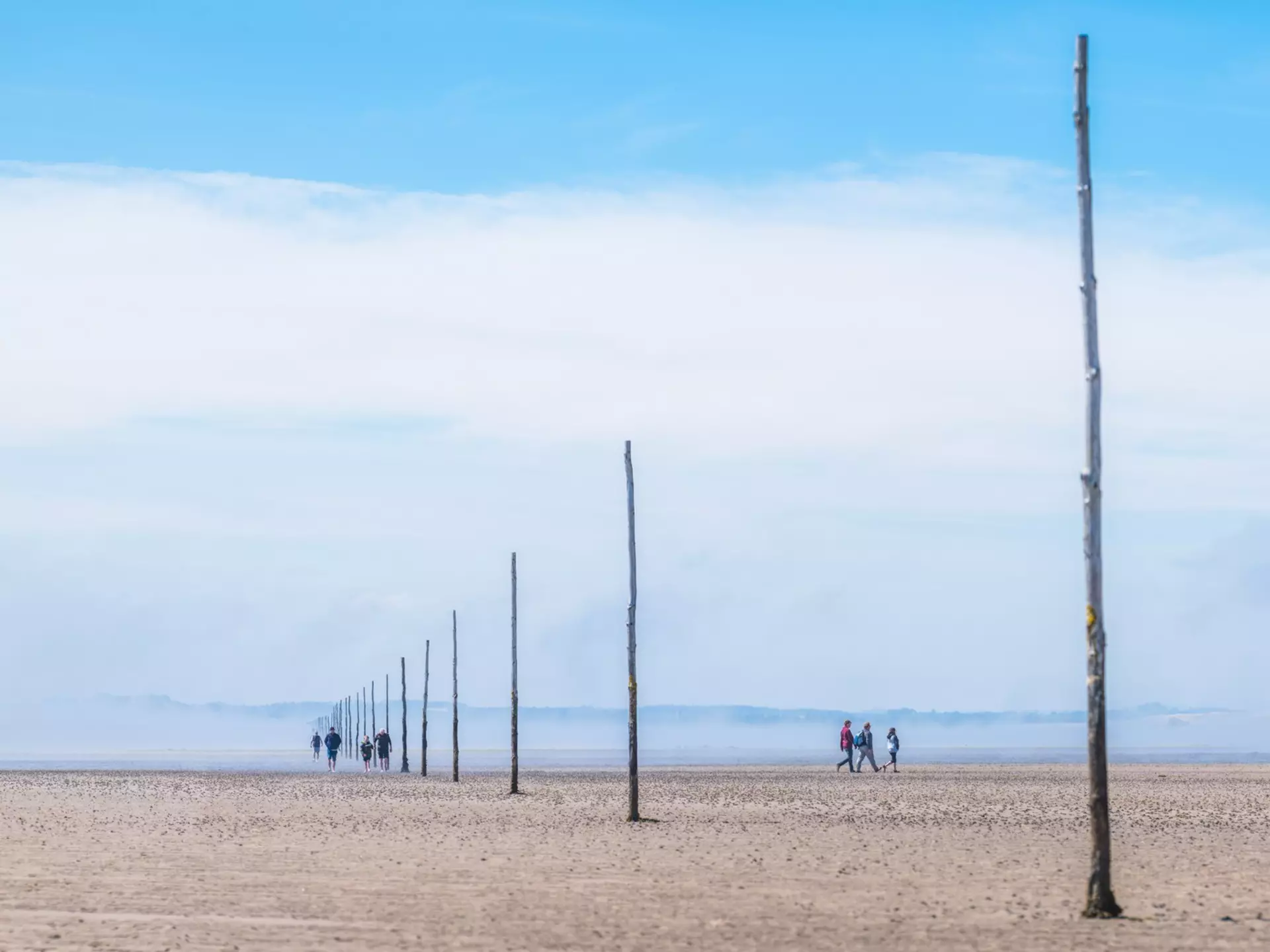 People walking along tidal mud flats in a vast expanse of emptiness, on the Pilgrim's Way to Holy Island, Lindisfarne, England