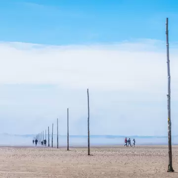 People walking along tidal mud flats in a vast expanse of emptiness, on the Pilgrim's Way to Holy Island, Lindisfarne, England