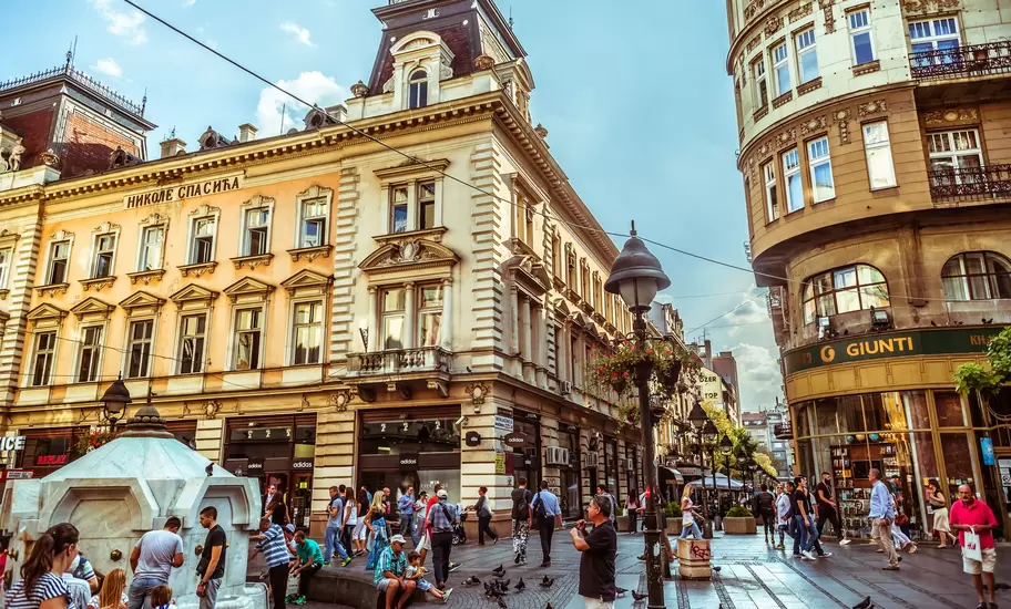 Knez Mihailova street in Belgrade, ornate buildings, one lettered НИКОЛЕ СПАСИЋА, and people at a white stone fountain