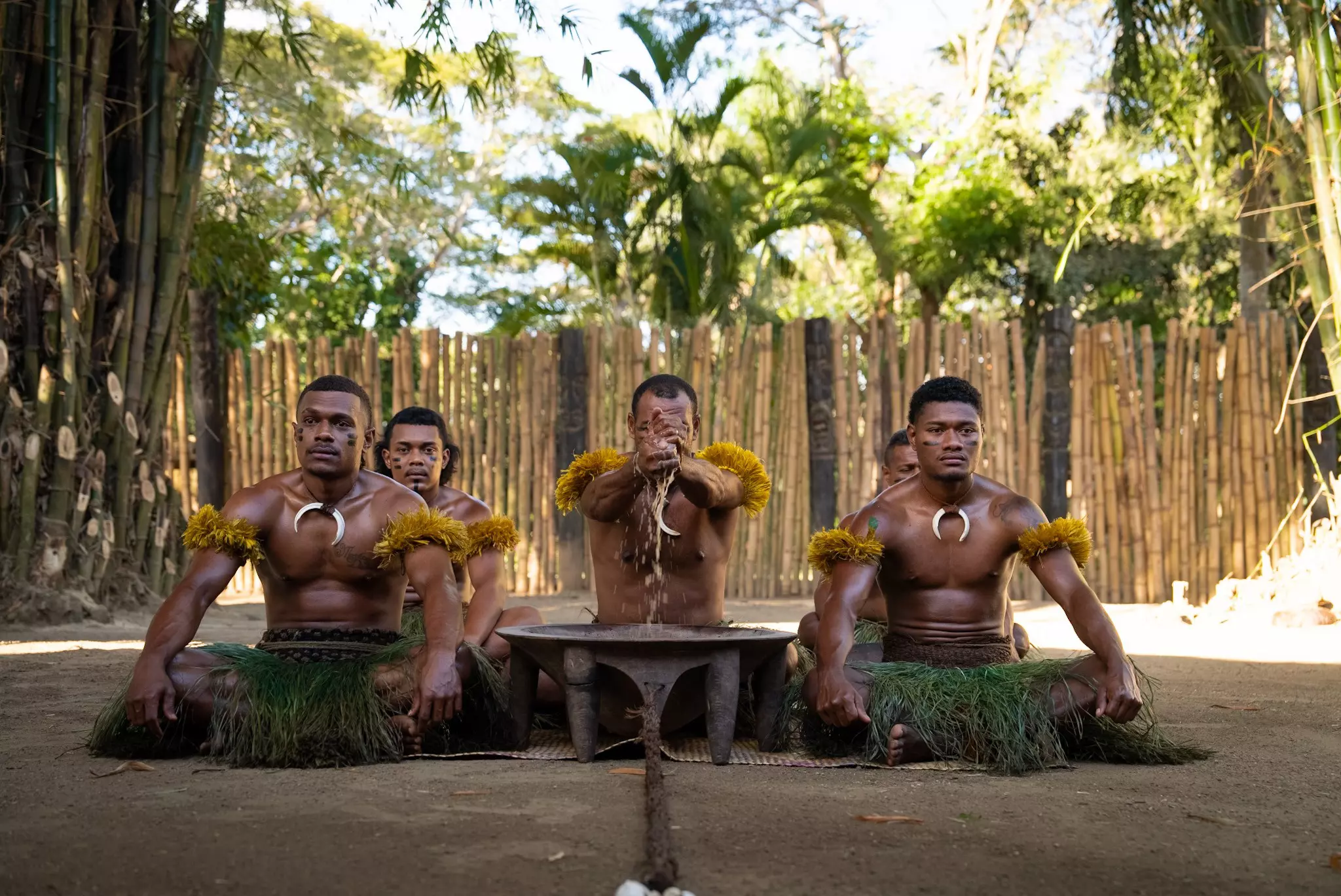 A traditional Kava ceremony in Nadi, with men seated outdoors and wearing grass skirts, necklaces and decorative yellow armbands