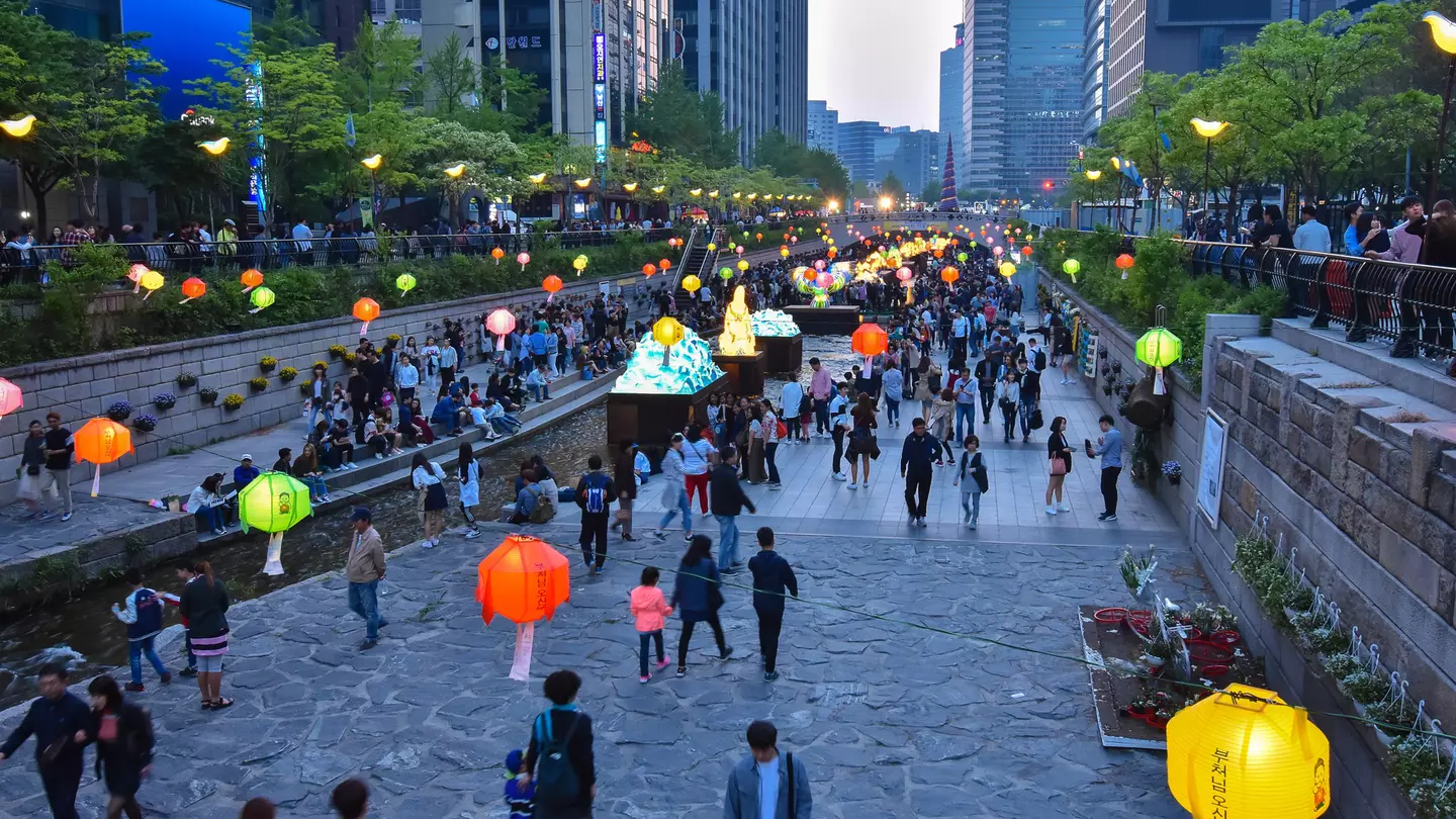 Paper lanterns hang over a public park and promenade in the built-up central business district of a city.