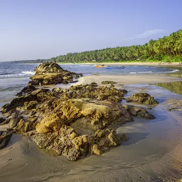 Kannur, December 10, 2011: Sunbathers and fishermen with boats on Cherai beach showing rocks formations in the foreground and coconut palms as backdrop at sunset along Malabar coastline, Kannur, Kerala, south India.