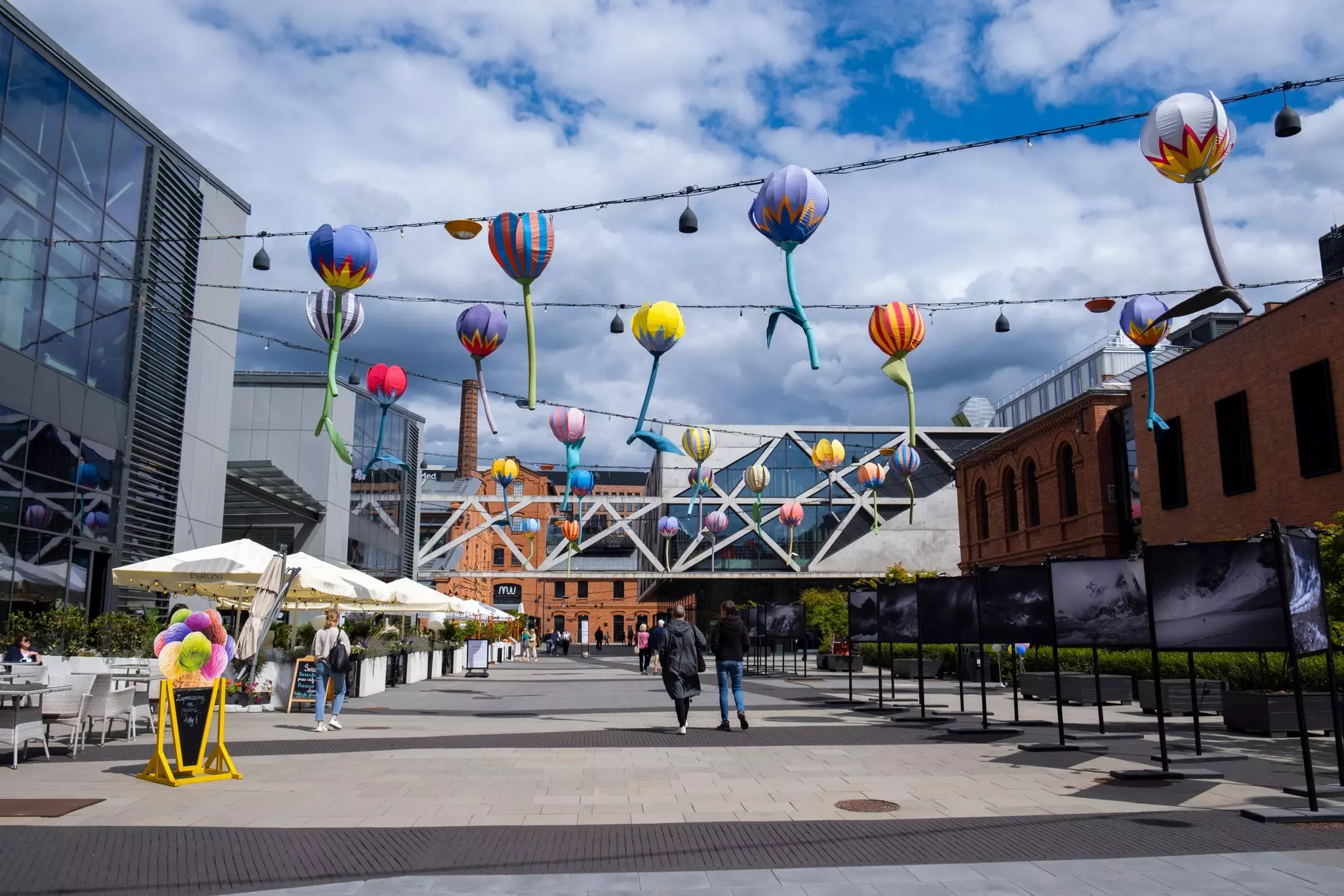 People walking through a wide pedestrian plaza in Poland with colorful objects strung overhead.