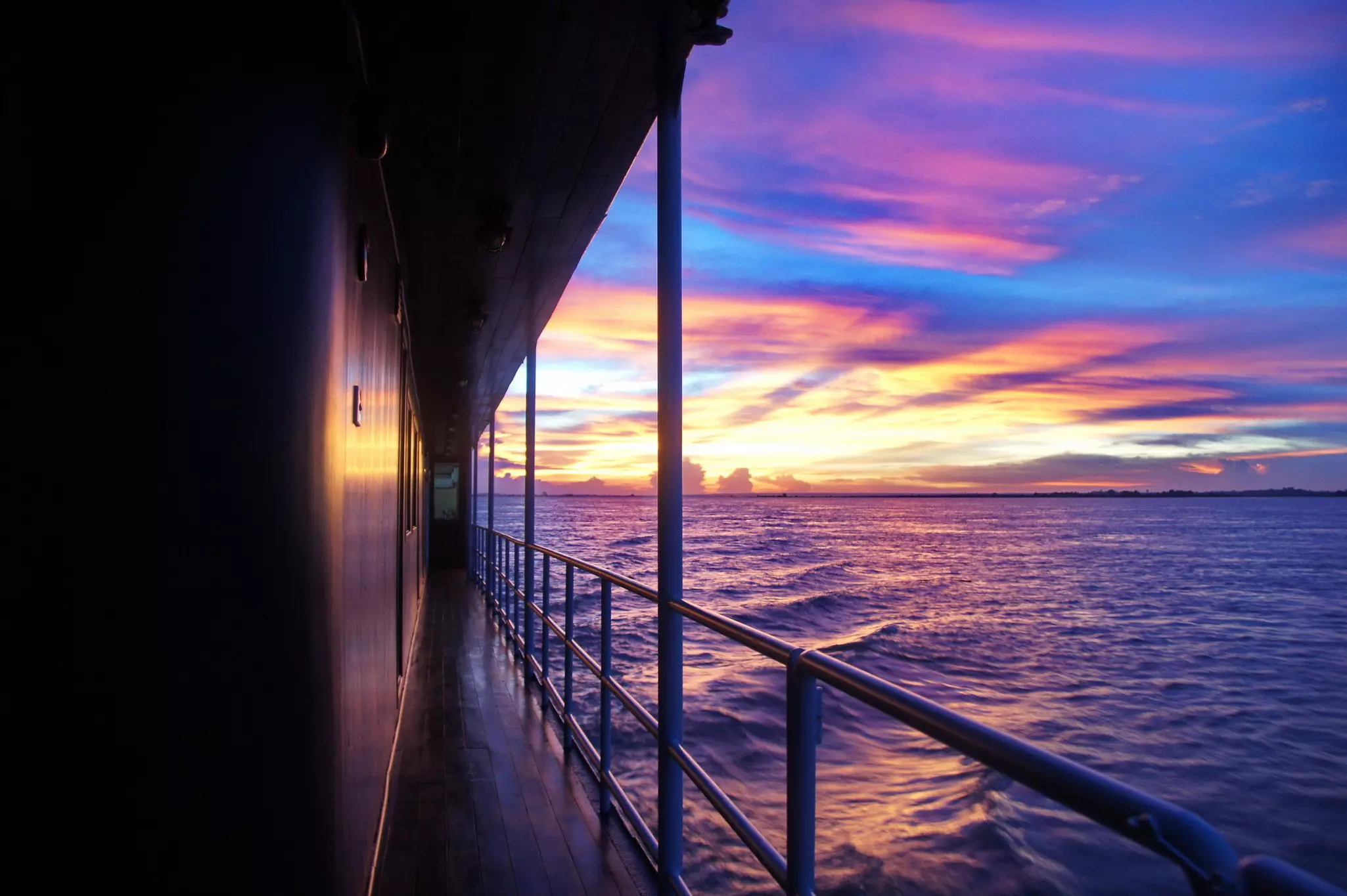 Sunset out over the water viewed from a passageway on the deck of a boat.
