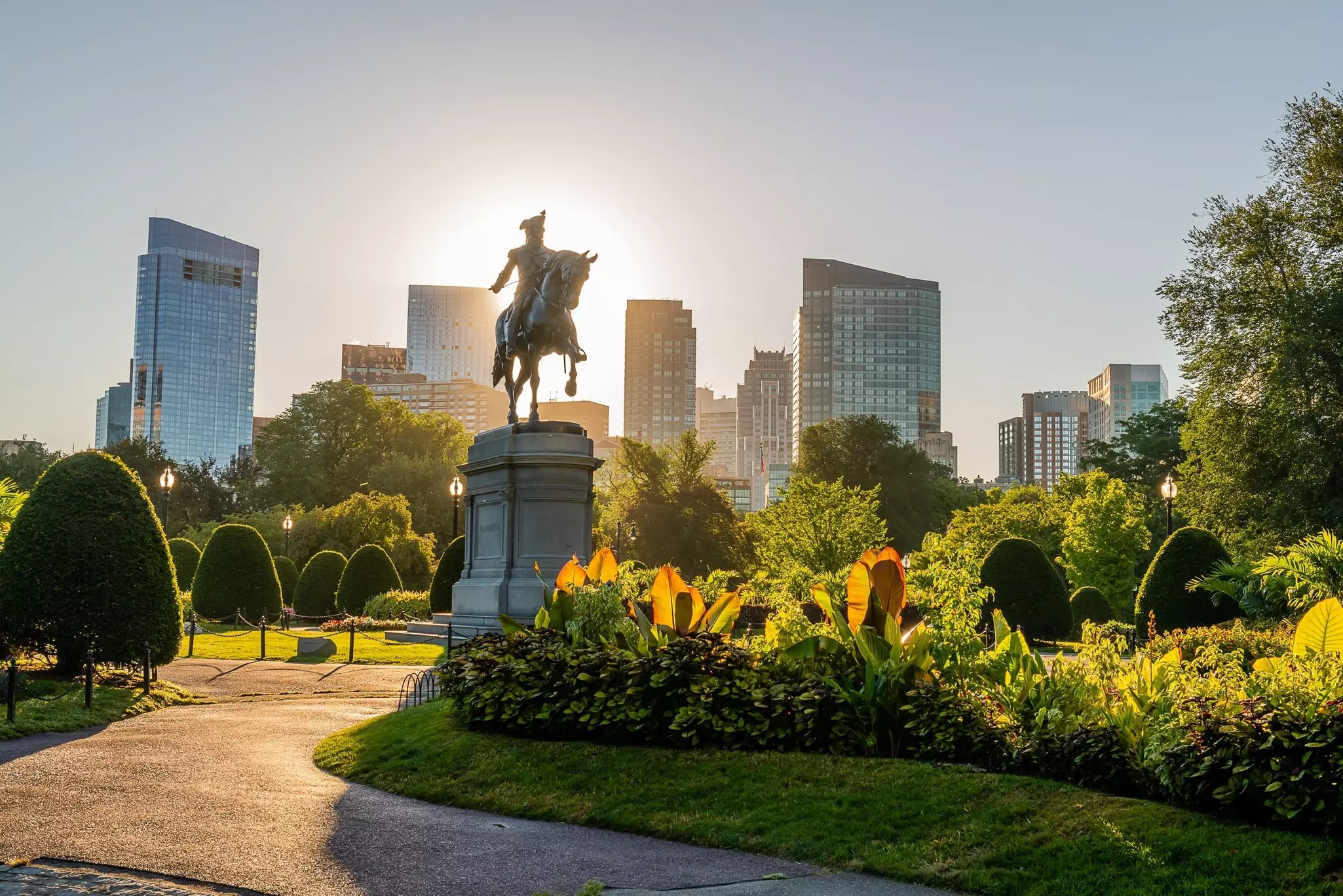 A statue of a man on horseback is the centerpiece of a city plaza lined with trees. The white spire of a church is seen in the background.