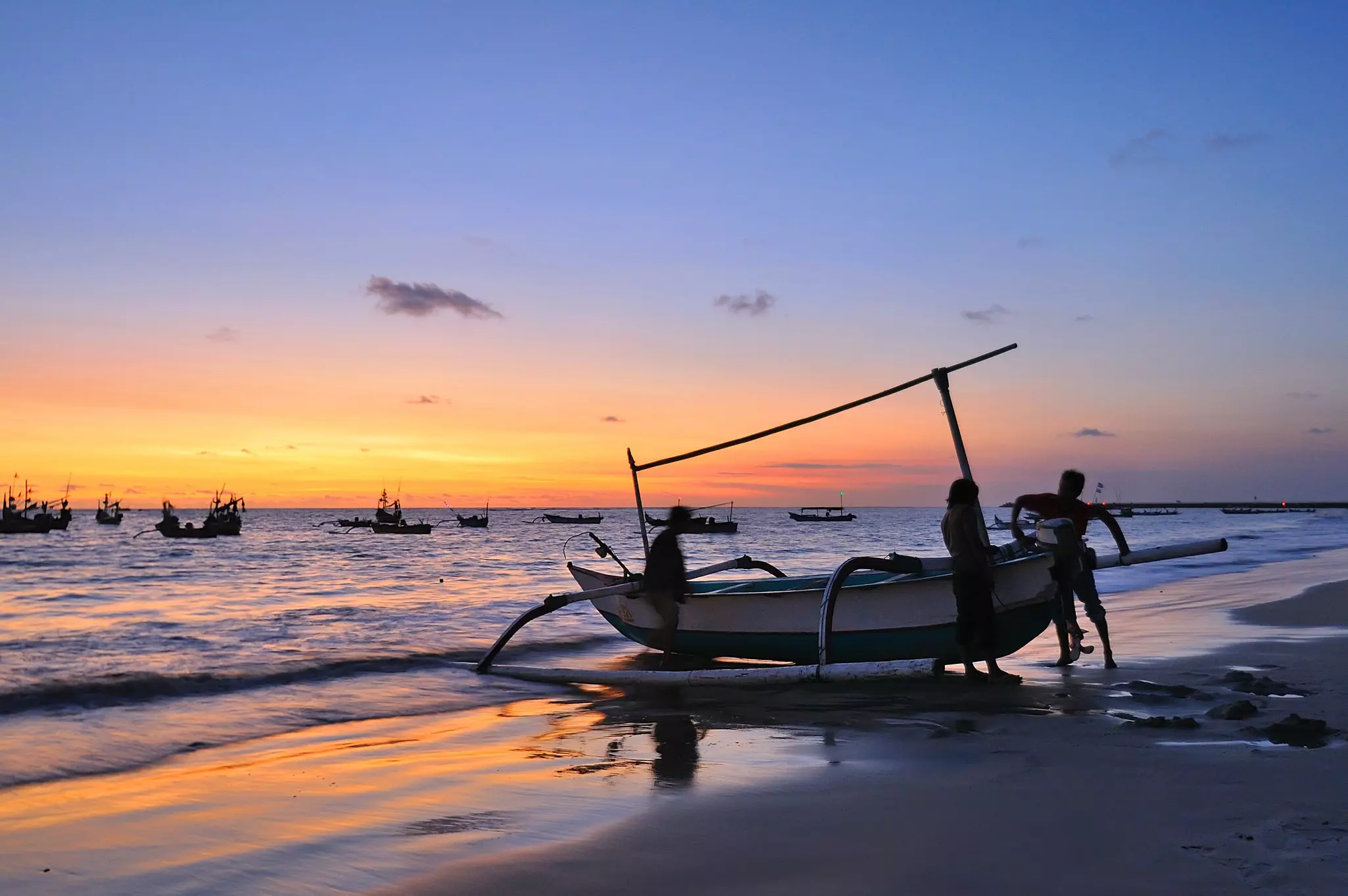 Deep orange, purple and yellow sunset in the sky and reflected on the water and sand at Jimbaran Beach