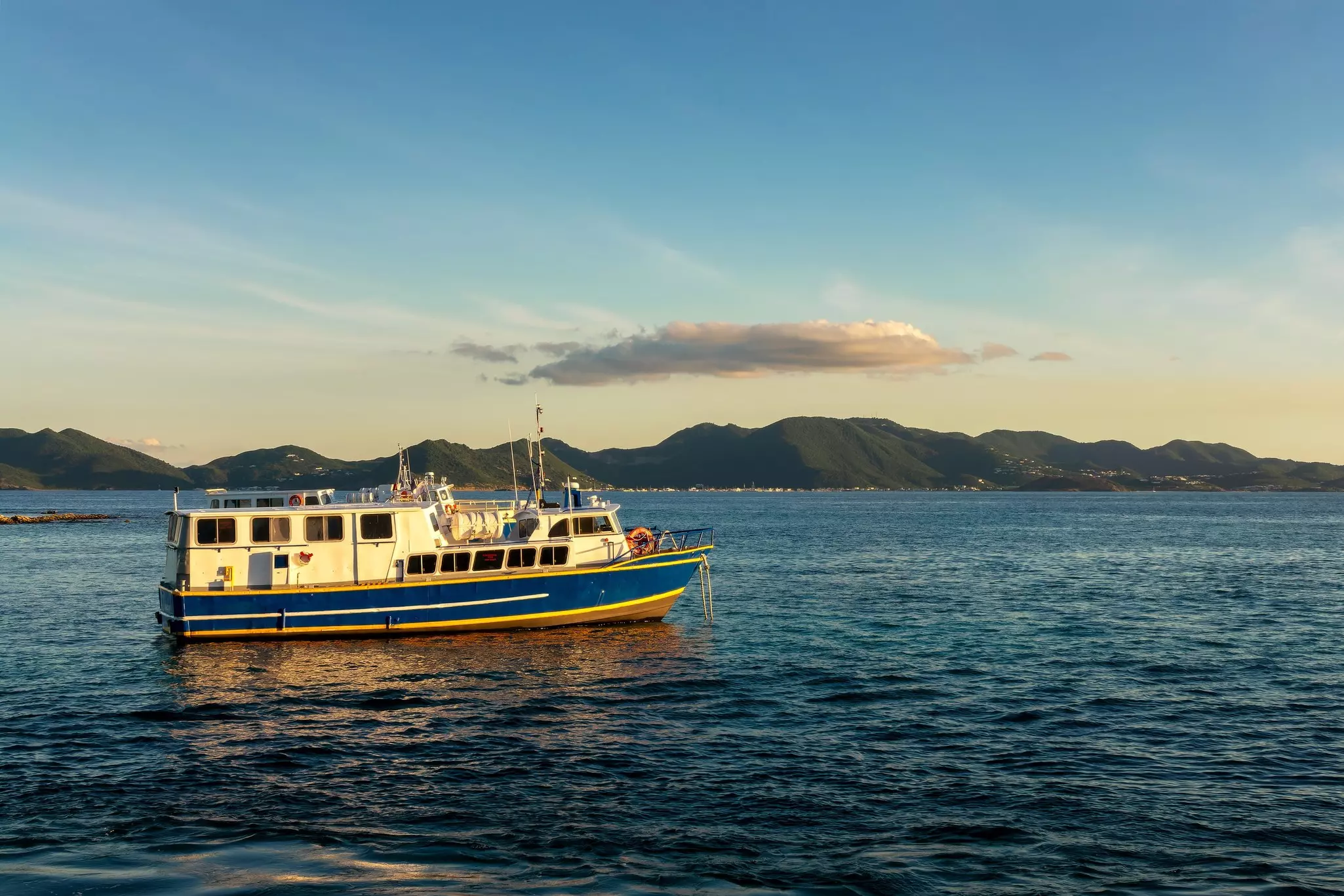 A small passenger ferry on dark blue water at sunset, with low, forested mountains in the distance.
