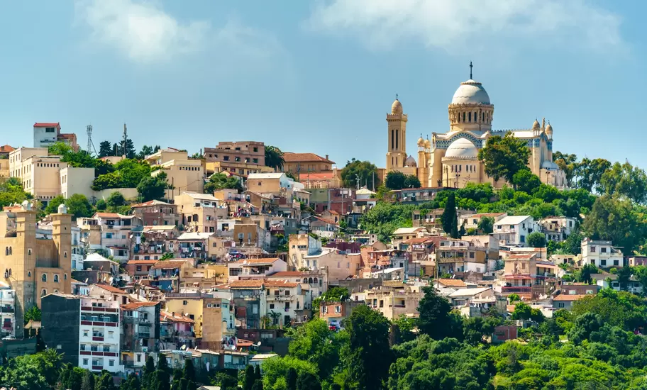 Notre-Dame d'Afrique basilica with its silver dome rises above dense hillside housing and trees in Algiers, Algeria