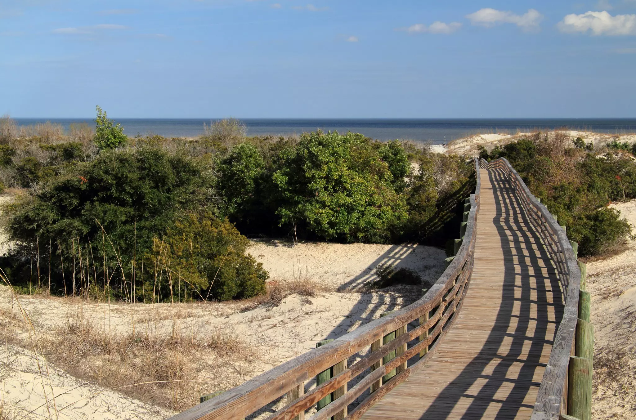A wooden boardwalk leads over sandy dunes towards the ocean.